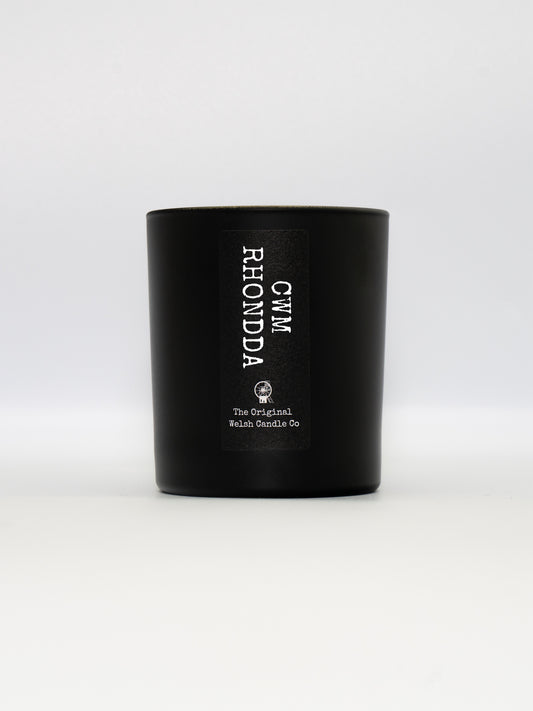 a matt black glass jar with a label saying CWM RHONDDA, filled with a luxury soy scented candle