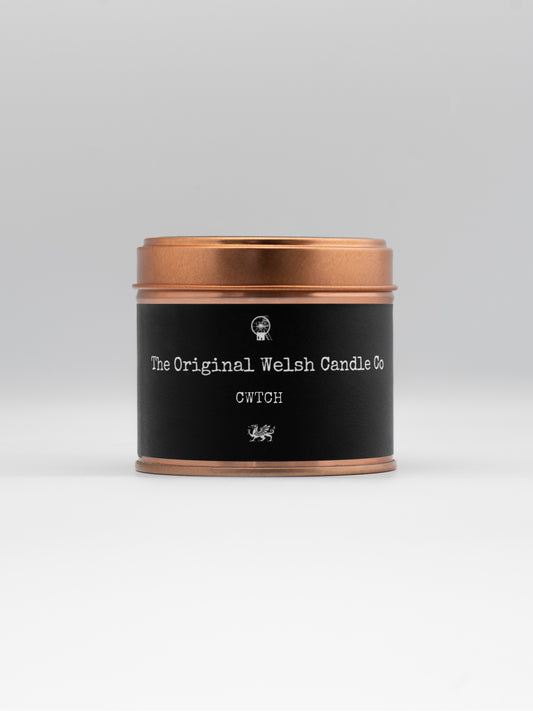 A cooper tin, labeled in black with CWTCH, conatins a luxury soy candle scented with rose and oud