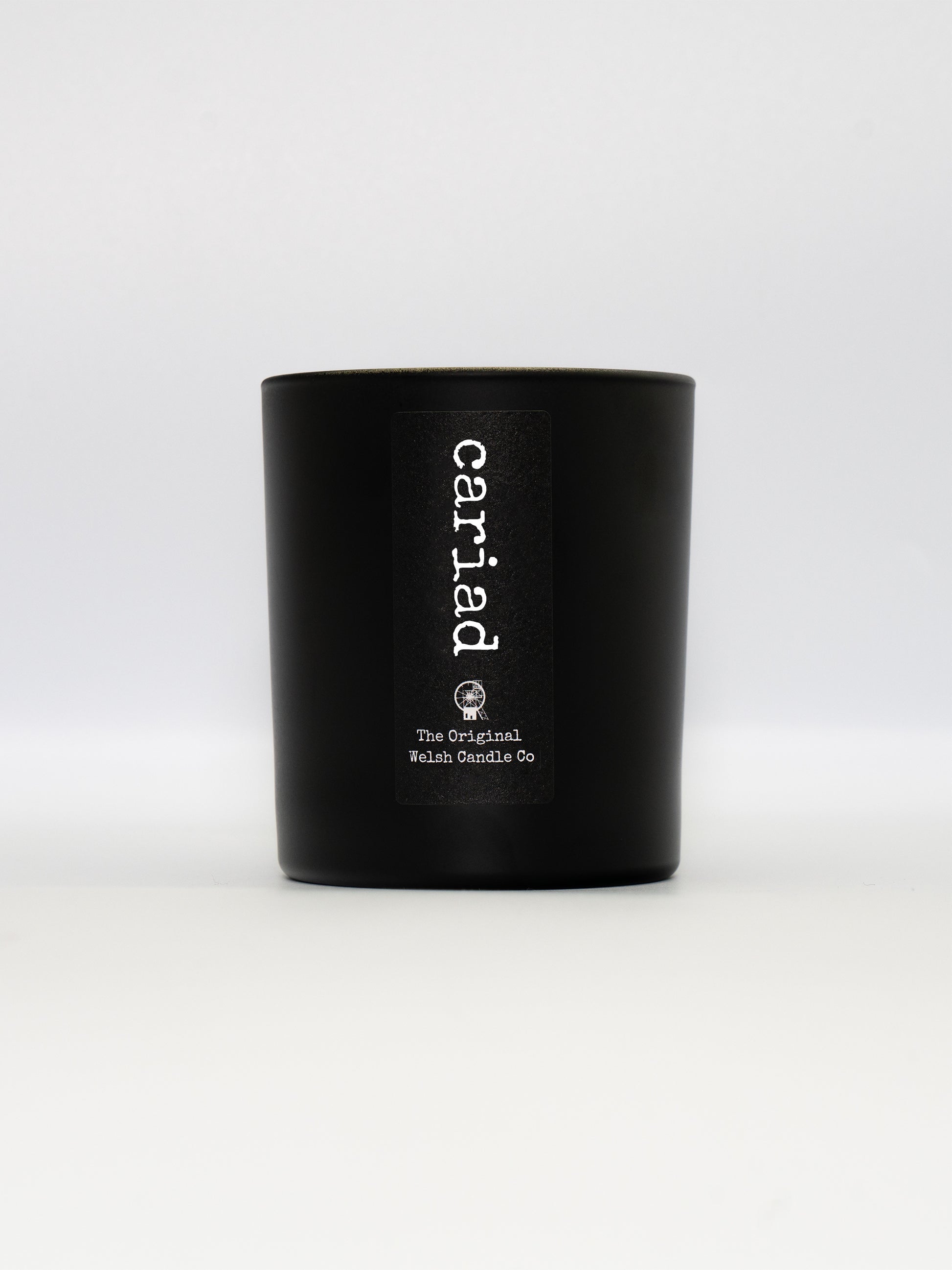 A matt black glass jar with a label saying cariad, filled with a black pomegranate soy candle