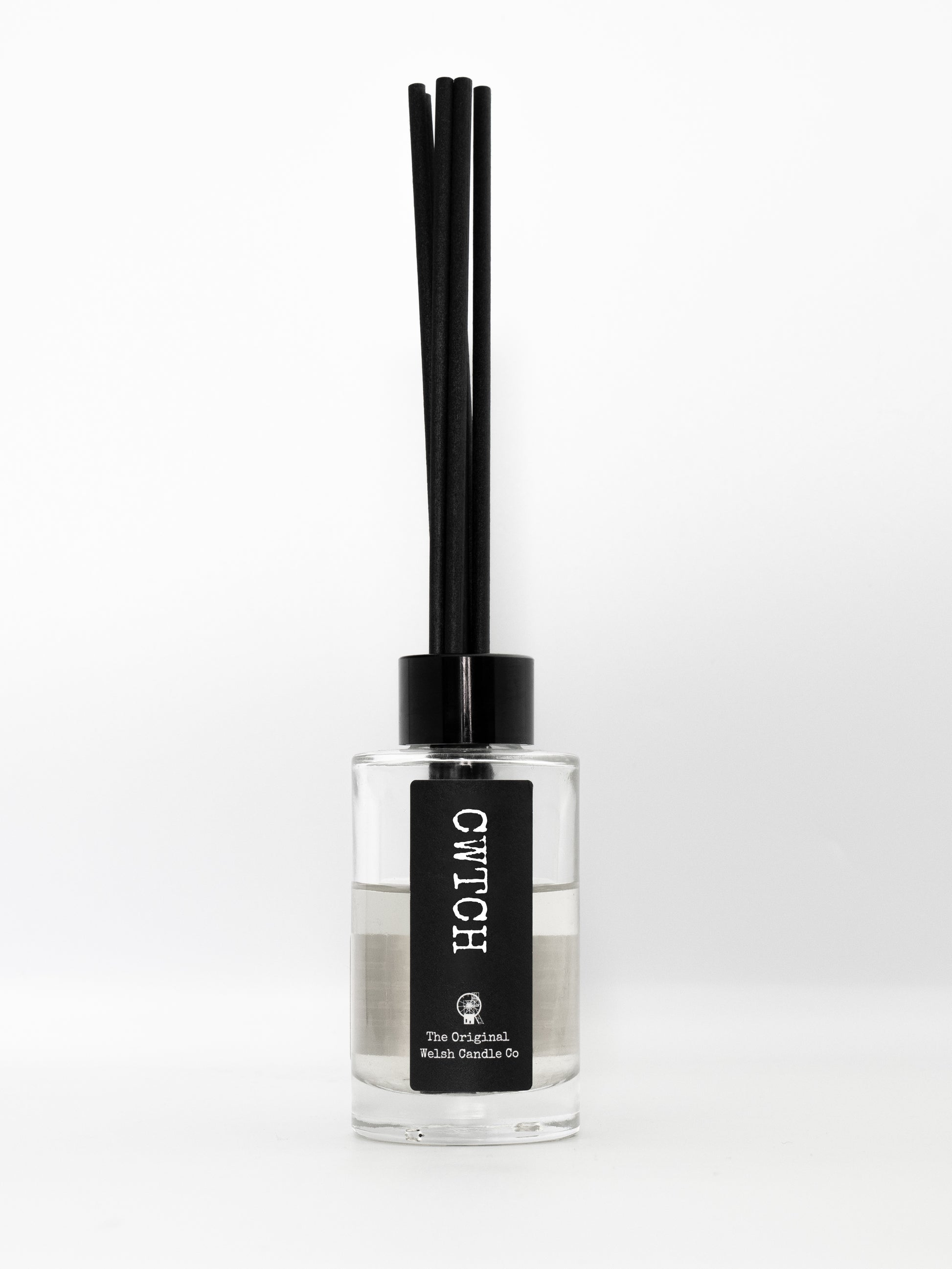 A clear bottle containing natural diffuser scented with rose and oud, has a cwtch label on the front and 7 black diffuser reeds