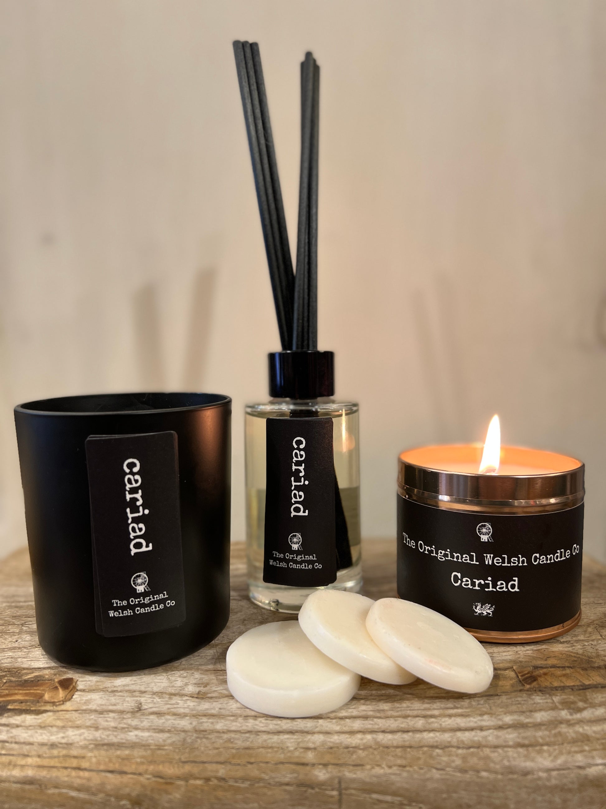 a gift box containing a glass reed diffuser, a matt black glass candle a copper tin candle and a pack of wax melts all scented with black pomegranate all labelled cariad